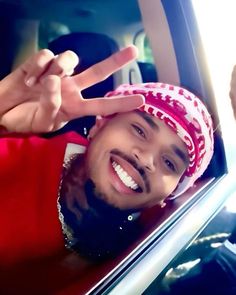 a man in a red shirt is making the peace sign with his hand while sitting in a car