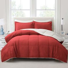 a red comforter set in front of a window with white pillows and blankets on it