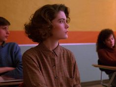 three young people sitting at desks in a classroom with one looking off to the side