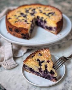 a blueberry cheesecake on a white plate with a slice cut out and ready to be eaten