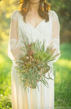 a woman in white dress holding a bouquet filled with flowers and greenery on her wedding day