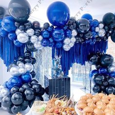 a table topped with lots of balloons next to a black and white dessert bar covered in blue tassels