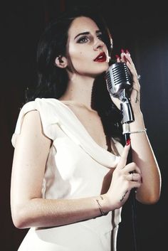 a woman in a white dress holding a microphone up to her face and looking off into the distance