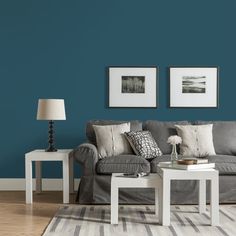 a living room with blue walls and two white tables in front of the couches