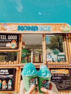 two ice cream cones are being held up in front of a kiosk stand