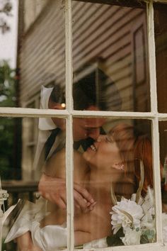 a man and woman kissing in front of a window