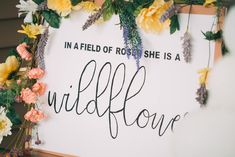 a sign that says in a field of roses she is a wildflower with flowers around it