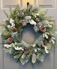 a wreath with pine cones and evergreens on the front door is decorated for christmas