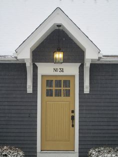 a yellow door sits in front of a gray house with snow on the ground and grass