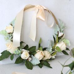 a wreath with white roses and greenery hanging on the wall next to a ribbon