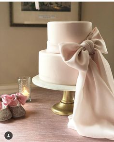 there is a wedding cake with pink bows on it and two baby shoes next to it