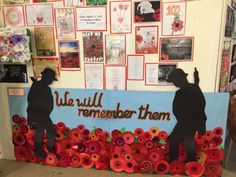 two people are standing in front of a wall with flowers and pictures on it that say we will remember them