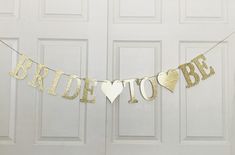 a bride to be banner hanging from a door with gold glitter hearts and the words bride to be on it