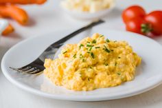 scrambled eggs on a white plate with a fork and some tomatoes in the back ground