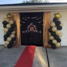 an entrance to a party decorated with black and gold balloons, streamers and red carpet