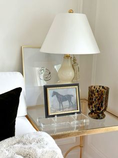 a glass table topped with a lamp next to a white chair and a framed photo