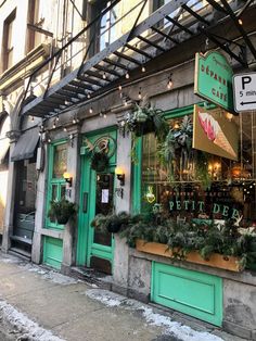 the outside of a restaurant with green doors and plants on display in front of it