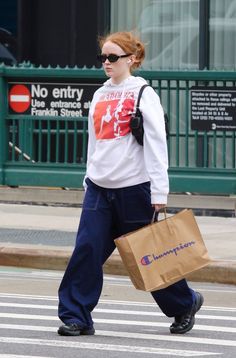 a woman walking across the street with a shopping bag in her hand and wearing sunglasses