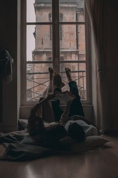 two people laying on the floor in front of a window with their feet propped up