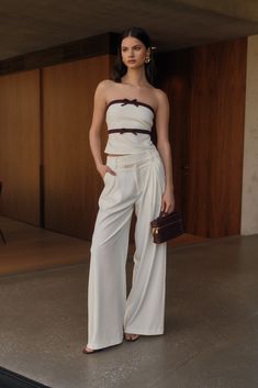 a woman standing in front of a wall wearing white pants and a strapless top