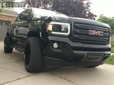 a black truck is parked in front of a garage with its lights on and it's hood up