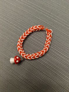 an orange and white braided bracelet with a red heart charm on it's end