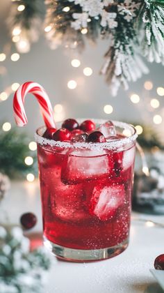 a red drink with candy cane on the rim in front of christmas decorations and lights