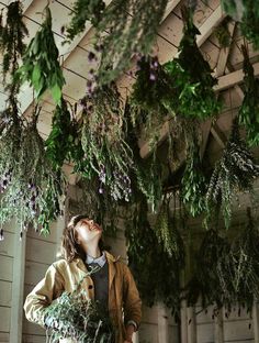 a woman standing in front of a bunch of greenery hanging from the side of a building