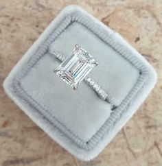 an emerald - cut diamond ring sits in a velvet box on top of a marble surface