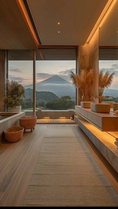 a room with large windows overlooking the mountains and water at sunset or sunrise, is lit up by lights that are on either side of the glass doors