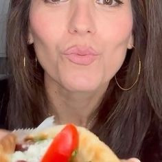 a woman holding a hot dog with toppings on it and looking at the camera