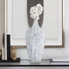 a white vase with flowers sitting on top of a table next to a book shelf