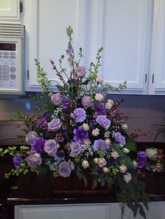 a vase filled with purple flowers sitting on top of a counter next to a microwave