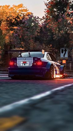 a blue sports car driving down the road in front of trees with orange leaves on it