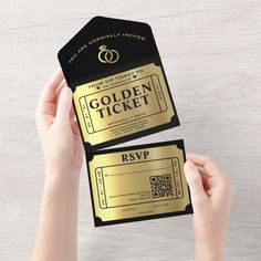 two gold ticket cards being held in front of a person's hand on a white table