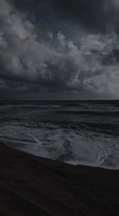 a person standing on the beach with a surfboard in their hand under a cloudy sky