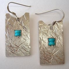 two square silver earrings with turquoise beads on them are sitting next to each other in front of a white background