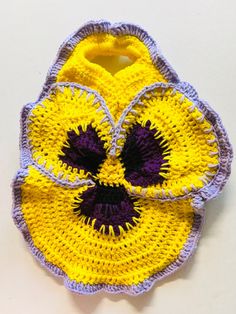 a crocheted yellow and purple flower on a white table with a black center