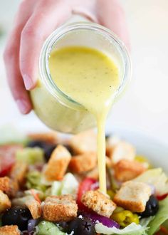 someone pouring dressing into a salad with croutons