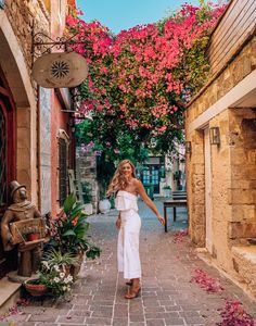 a woman in white dress walking down an alley way with flowers growing on the walls