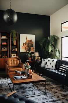 a living room with black walls and leather couches, coffee table, potted plants and bookshelves