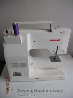 a white sewing machine sitting on top of a table next to a purple thread spool