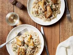 two white plates topped with pasta and chicken next to silverware on a wooden table