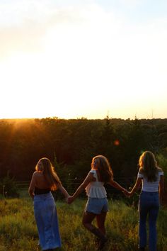 three girls are holding hands in a field