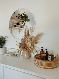 a white dresser topped with lots of bottles and vases next to a round mirror