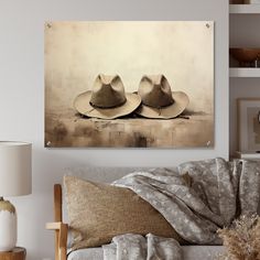 two hats sitting on top of a couch in front of a wall mounted art piece