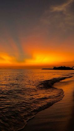 the sun is setting over the ocean with waves coming in to shore and an island in the distance