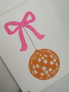 an orange ornament with a pink bow hanging from it's side on a white card