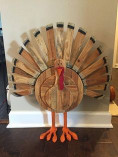 a wooden turkey with orange feet standing in front of a white wall and wood floor