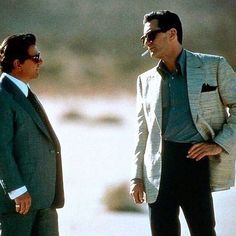 two men standing next to each other in suits and sunglasses, one is looking at the other